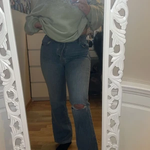 Blå jeans från H&M - Säljer ett par klassiska blå jeans från H&M. De har en straight passform och är högmidjade med knappar framtill. Perfekta för en avslappnad stil med en snygg slitning på knäet.