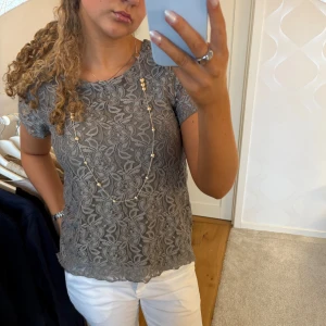 Grå/ grön spetsblus - Säljer en elegant grå/ gröna spetsblus med korta ärmar och ett vackert blommönster. Perfekt för att ge en stilren touch till din outfit. använd fåtal gånger och är i bra skick🥰
