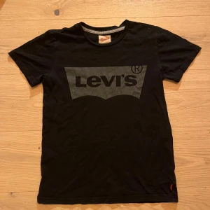 Svart t-shirt från Levi's - Snygg svart t-shirt från Levi's med det klassiska logotyptrycket i grått på framsidan. Perfekt för en casual look. T-shirten har korta ärmar och en rund halsringning.