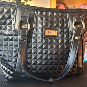 Fin väska från Feel! - Fin svart väska i fuskskinn med handtag, justerbar axelrem, flera fack och dragkedja. Mått: 25 x 35 cm. I kanonskick!