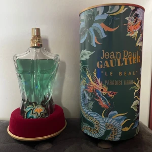 Jean Paul Gaultier Le Beau Eau de Toilette - Säljer en Jean Paul Gaultier Le Beau Eau de Toilette. Flaskan har en unik design formad som en manlig torso i genomskinligt glas med en grön vätska inuti. Den kommer med en dekorativ förpackning med tropiskt tema och drakmotiv. Perfekt för den som vill ha en fräsch och exotisk doft.