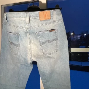 Ljusblå jeans från Nudie Jeans - Snygga ljusblå jeans från Nudie Jeans med klassisk femficksdesign. De har en normal passform och är tillverkade i slitstarkt denim. Perfekta för en avslappnad stil. Jeansen är fläk fria och sparsamt användna. Jeansen är i storlek w 30 L 32. Priset är ej hugget i sten och går att pruta vid snabb affär
