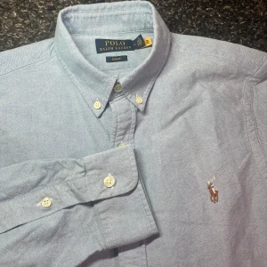 Ralph Lauren skjorta  - Snygg blå skjorta från Ralph Lauren i slim fit. Skjortan har långa ärmar och klassiska knappar framtill. Den är broderad med den ikoniska loggan på bröstet. Perfekt för både vardag och fest! Cond 9/10. Extremt snyggt plagg nu till sommaren! Hör av dig vid minsta lilla fråga!🤩