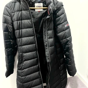 Svart lång  dunjacka från Tommy Hilfiger -  svart lång dunjacka från Tommy Hilfiger, använt en vinter. Storlek M men jag som i vanliga fall hae xs/s tyckte den passa jättebra. Jättebra skick inga fel. Nypris 3195kr