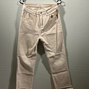 Beige jeans från Oraije - Snygga beige jeans från Oraije med en avslappnad passform. Byxorna har en klassisk femficksdesign och råa kanter vid bensluten för en trendig look. Perfekta för en stilren vardagsoutfit.
