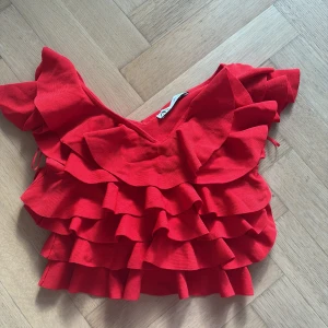 Röd volangtopp från Zara - Säljer en snygg röd volangtopp från Zara. Toppen har flera lager av volanger och korta ärmar, vilket ger en festlig look.