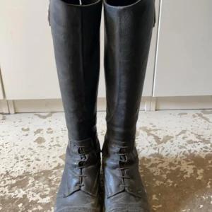 Svarta ridstövlar från CRW - Säljer ett par svarta ridstövlar från CRW i läder. Stövlarna har snörning framtill och dragkedja baktill för enkel på- och avtagning. Perfekta för hobbyridning. Finns lite slitage & repor då de är väl använda men håller ett bra tag till vid endast hobbyridning.
