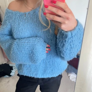 Blå stickad tröja - Mysig blå stickad tröja med en avslappnad passform. Tröjan har en offshoulder-design och långa ärmar, perfekt för kyligare dagar. Den fluffiga texturen ger en extra touch av komfort och stil.