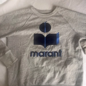  Isabel Marant - Säljer en stilren grå sweatshirt från Isabel Marant med ett stort blått tryck på framsidan. Tröjan har långa ärmar och en rund halsringning. Perfekt för en avslappnad look. Så fin verkligen🩷🩷