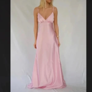 Sophie dress By Stina - Elegant ljusrosa långklänning i satin med smala axelband och v-ringad hals. Perfekt för speciella tillfällen med sin mjuka och glänsande yta. Säljer för att jag hittat en annan balklänning🥰 Aldrig använd! Skriv för fler bilder