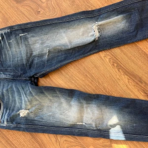 Replay anbass jeans - Snygga blå jeans från Replay med slitna detaljer och en cool röd dragkedja vid fickan. Perfekta för en avslappnad stil. De har en klassisk femficksdesign och en bekväm passform. Passformen är anbass (slim fit). Topp skick, inga defekter. Pris: 499