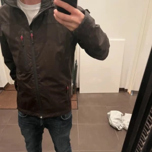 Svart jacka från Helly Hansen - Säljer en svart jacka från Helly Hansen med dragkedja och HH-logga på ärmen. Den är Hydropower vilket är en lite varmare modell på jackan än den vanliga tunna vindjackan.