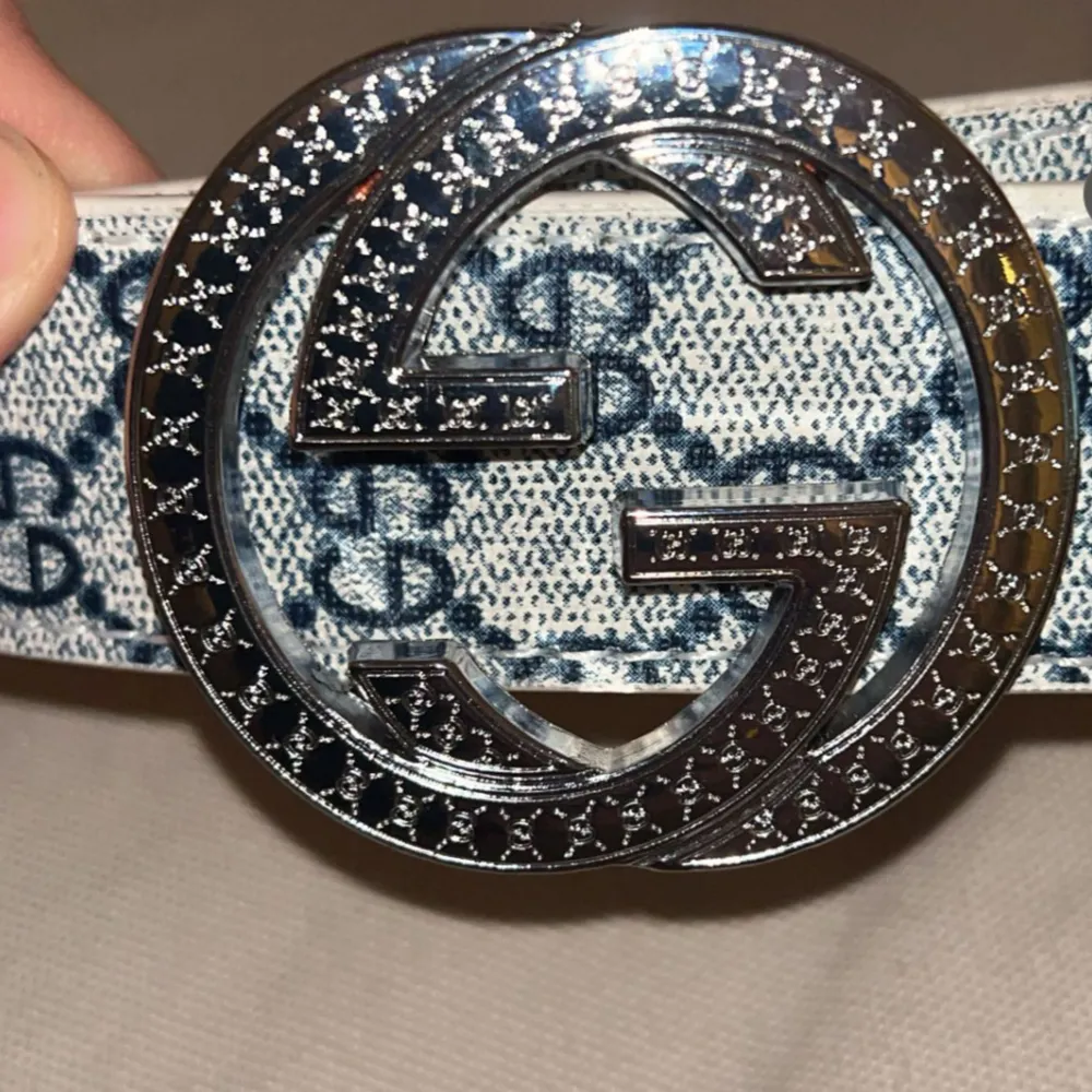 Snyggt vitt bälte från Gucci med ett marinblått mönster på. Bältet har en stor, rund spänne i silver med det ikoniska GG-emblemet. Perfekt för att ge en lyxig touch till din outfit.. Asusteet.