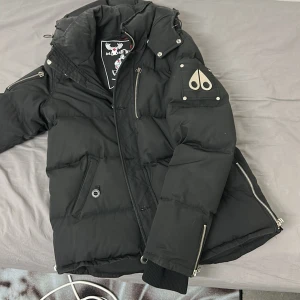 Svart dunjacka från Moose Knuckles - Säljer en svart dunjacka från Moose Knuckles med coola detaljer som dragkedjor och ett märke på ärmen. Jackan har en quiltad design och är perfekt för kalla dagar. Den har långa ärmar och en skön huva för extra värme. Perfekt för Sveriges väder! 🖤köpte den för 4500 i vintras, priset kan diskuteras vid snabbaffär.
