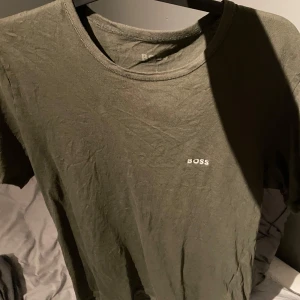 Olivgrön  t-shirt från Hugo  Boss - Säljer en stilren olivgrön t-shirt från Boss. Den har en klassisk rund halsringning och korta ärmar. Perfekt för en avslappnad look.