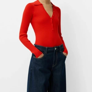 Röd ribbad tröja med öppen rygg - Snygg röd ribbad body tröja med lång ärm och knappar framtill. Tröjan har en djup v-ringning och en trendig öppen rygg. Perfekt för att ge en stilren look med en twist. Helt oanvänd med prislapp kvar. Från Bershka.