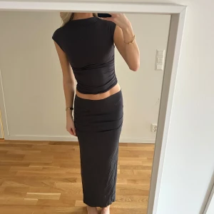 Set med kjol och topp - Snyggt mörk grått set med långkjol och topp med korta ärmar och hög hals. Settet är figurnära och framhäver formerna på ett smickrande sätt