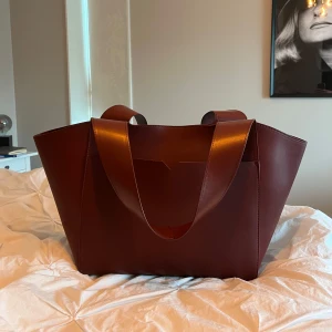 Röd väska Carin Wester - Väska från Carin Wester som inte kommit till användning mer än en gång.                                                 Mått:                                               Bredd nedtill: 35 cm Bredd upptill: 60 cm Höjd: 32 cm Djup: 14 cm