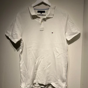 Vit pikétröja från Tommy Hilfiger - Säljer en klassisk vit pikétröja från Tommy Hilfiger. Tröjan har en liten logotyp på bröstet och en traditionell krage med knappar. Perfekt för en stilren och avslappnad look.
