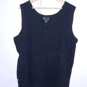 Svart ärmlös topp från Ralph Lauren - Säljer en klassisk svart ärmlös topp från Ralph Lauren. Tillverkad i 100% bomull, perfekt för en stilren look. Toppen har en enkel design med rund halsringning och en liten knytning framtill.