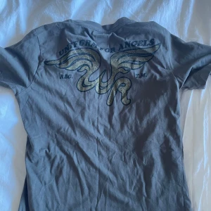 Grå t-shirt från Replay - Säljer en grå t-shirt från Replay med tryck 'Uniform for Angels' och vingmotiv på både fram- och baksidan. T-shirten har en normal passform och är kortärmad. Perfekt för en avslappnad stil.