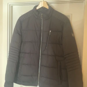 Jofama - Svart quiltad jacka med dragkedja - Säljer en svart jacka i mycket bra skick. Den har en dragkedja framtill och en praktisk bröstficka med dragkedja. Perfekt för höst och vinter, med långa ärmar och en stilren look. Passar både till vardags och lite finare tillfällen.