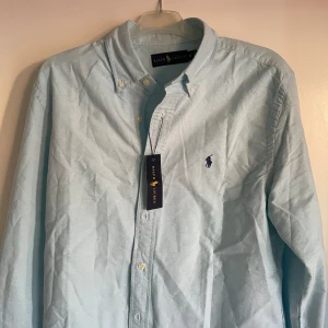 Ljusblå skjorta från Ralph Lauren - Säljer en snygg ljusblå skjorta från Ralph Lauren i storlek M. Skjortan är i nytt skick med etikett kvar. Den har långa ärmar och klassiska knappar framtill. Perfekt för både vardag och fest! 💙