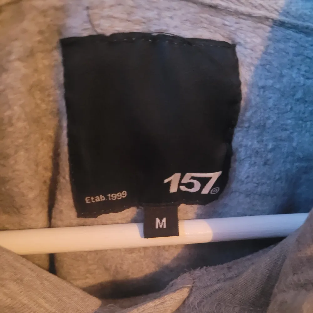 Säljer en grå hoodie från 157 i storlek M. Den är supermjuk och perfekt för kyliga dagar. Hoodien har en klassisk design med snören i huvan och ribbade muddar vid ärmslut och nederkant. Perfekt för både vardag och mysiga hemmakvällar!. Tröjor & Koftor.