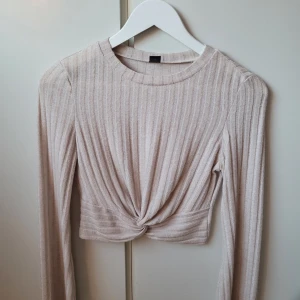 Beige ribbad topp från Shein - Säljer en superfin beige ribbad topp från Shein i storlek S. Den är croppad med en snygg knutdetalj framtill och har långa ärmar. Perfekt för både vardag och fest! 🥰