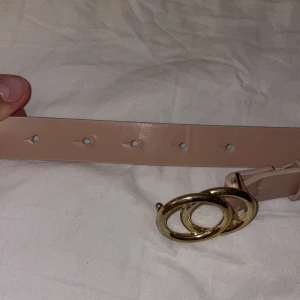 Beige bälte med guldfärgat spänne från H&M - Säljer ett stilrent beige bälte från H&M med ett elegant guldfärgat spänne. Perfekt för att piffa upp vilken outfit som helst. Bältet är i nyskick och passar bra till både vardag och fest. 