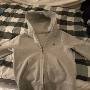 Grå hoodie från Polo Ralph Lauren - Säljer en snygg och bekväm grå hoodie från Polo Ralph Lauren. Den har en dragkedja framtill och en klassisk logga på bröstet. Perfekt för både vardag och chill. Passar bra till jeans eller joggers. Pris kan diskuteras.