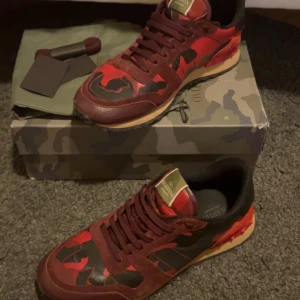 Valentino Rockrunner i röd och svart - Säljer ett par snygga Valentino Rockrunner sneakers i röd och svart camouflage. De har en cool design med snörning och är i mycket bra skick. 