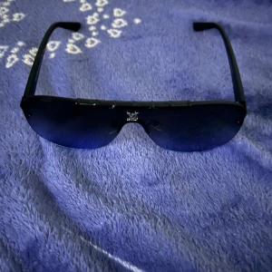 Svarta solglasögon från Louis Vuitton - Snygga svarta solglasögon från Louis Vuitton i ett sportigt och elegant utförande. De har en stilren design med mörka glas och en diskret logga på sidan. Perfekta för både vardag och fest! Tillverkade i Italien för en lyxig känsla. Passar bra till alla outfits och ger ett coolt intryck. 😎