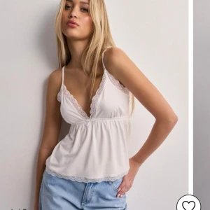 Vit spetskantad linnetopp - Säljer denna jättesöta vita linnetoppen med spetsdetaljer vid halsringningen och nederkanten. Toppen har smala axelband. Säljer då jag knappast använder den tyvärr. Har använts fåtal gånger. Dock så saknar toppen jag säljer rosett!