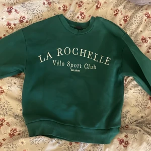 Grön sweatshirt från Gina tricot - Säljer en snygg grön sweatshirt från Gina tricot. Den har en klassisk rund hals och långa ärmar. Perfekt för en avslappnad stil eller sportiga dagar. Texten på framsidan ger en cool vintage-känsla. Passar perfekt till jeans eller träningsbyxor!