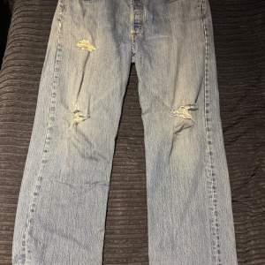 Säljer ett par klassiska blå Levis jeans med coola slitningar på framsidan. Perfekta för en avslappnad stil. De har en straight passform och är i bra skick trots slitningarna.