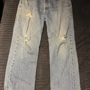 Säljer ett par klassiska blå Levis jeans med coola slitningar på framsidan. Perfekta för en avslappnad stil. De har en straight passform och är i bra skick trots slitningarna.