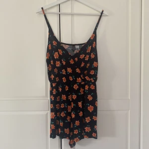 Svart jumpsuit med orangea blommor  - Söt jumpsuit med orangea blommor. Helt oanvänd. 🌼
