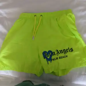 Säljer ett par supercoola neongula shorts från Palm Angels med en blå hjärtdetalj och texten 'Palm Beach'. De har en elastisk midja med gul dragsko för perfekt passform. Perfekta för sommardagar på stranden eller bara chilla runt i stan. 🏖️