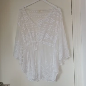 Vit spetsblus från Mirelle - Säljer en superfin vit spetsblus från Mirelle, tillverkad i Italien. Blusen har en v-ringad design med vackra broderade detaljer och ett knytband i midjan. Den är perfekt för sommarens alla fester och har en luftig och bekväm passform.