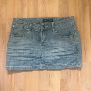 Jeanskjol från M.H.O Jeans - Säljer en snygg jeanskjol från M.H.O Jeans. Den är i en klassisk blå denimfärg och har en kort modell. Kjolen har två fickor fram och två bak, med en cool broderad detalj på ena bakfickan. En perfekt sommar outfit.