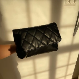 Svart quiltad kuvertväska - Säljer en superfin svart kuvertväska i quiltat skinn. Den har en elegant design med små knappar som ger en extra touch. Perfekt för skola och fest! 🖤