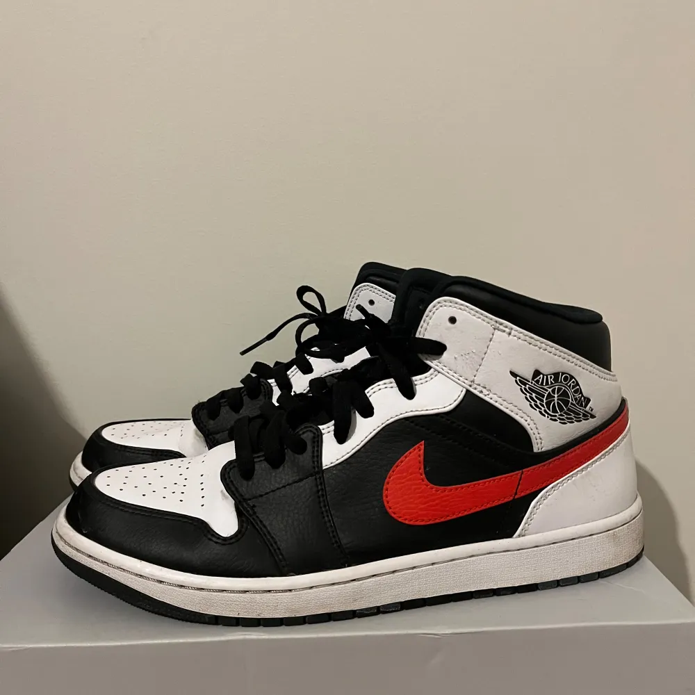 Säljer ett par snygga Nike Air Jordans i svart, vitt och rött. Skorna har en klassisk design med svart snörning och den ikoniska röda swooshen på sidan. Perfekta för både vardag och fest!. Skor.