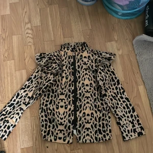 Leopardmönstrad jacka med volanger - Säljer en cool leopardmönstrad jacka med volanger på axlarna. Jackan är långärmad och har en dragkedja framtill. Perfekt för att sticka ut på festen eller bara för en trendig vardagslook!