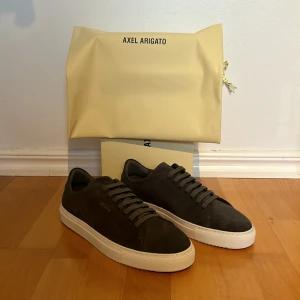 Axel Arigato Skor  - Säljer nu mina Axel Arigto CLEAN 90 SUEDE i dark grey. Skorna är helt nya och är aldrig använda som man kan se på bilderna. [Skick: 10/10] Storlek: 43 passar 42. [Kostar 2400:- i butik] [mitt pris: 1799:-]. Hör av er vid frågor och funderingar. 
