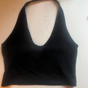 Svart ärmlös topp - Säljer en stilren svart ärmlös topp med djup urringning. Perfekt för sommardagar eller en utekväll. Toppen är tight och croppad, vilket ger en snygg och modern look.