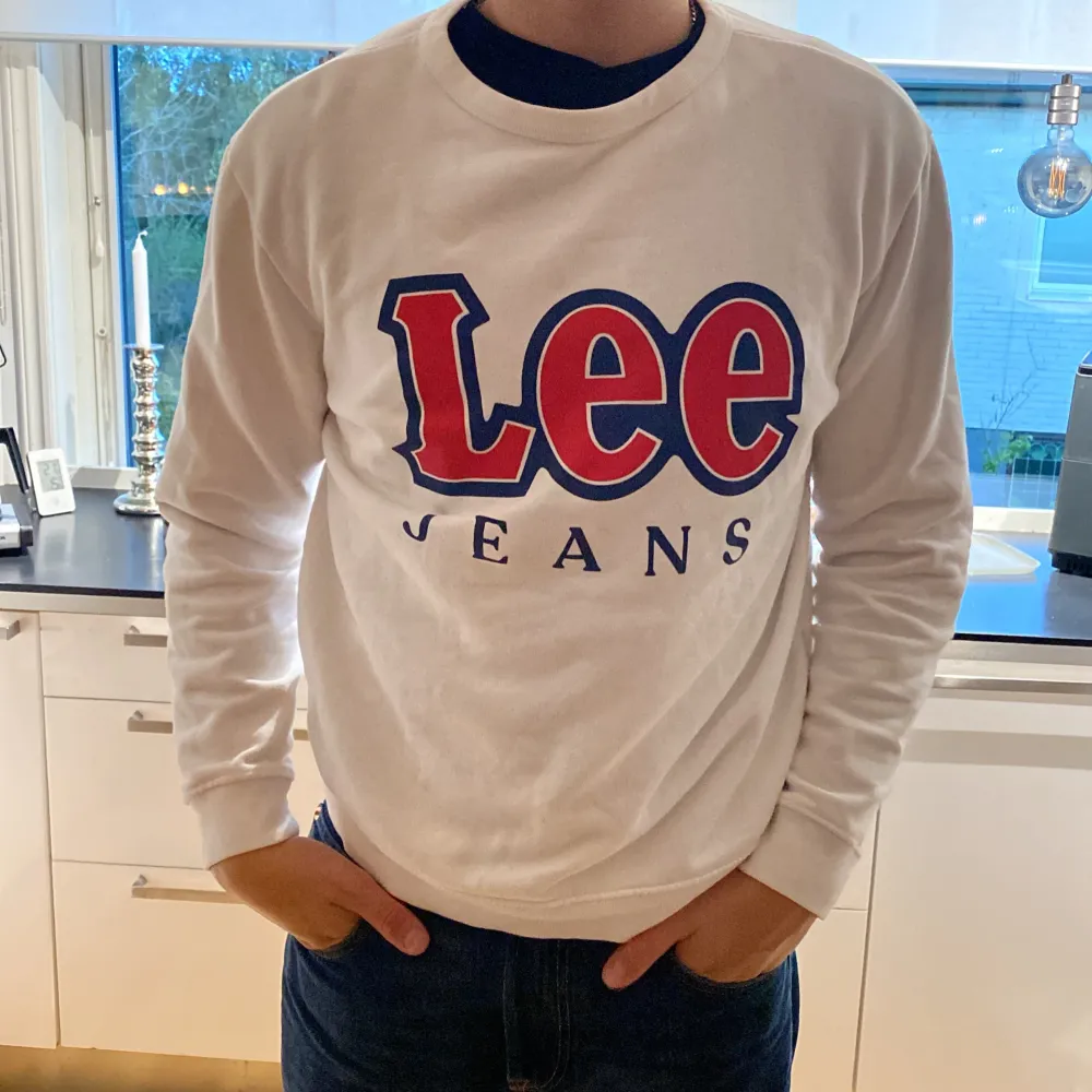 Säljer en snygg vit sweatshirt från Lee med deras klassiska logga i rött och blått på framsidan. Tröjan är långärmad och perfekt för en casual look. Den är i storlek L och i bra skick. Perfekt för höst och vår!. Hoodies.