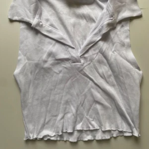 Vit ärmlös topp från Pull&Bear - Säljer en vit ärmlös topp från Pull&Bear i storlek S. Toppen har en enkel och stilren design med en liten v-ringning med krage. Perfekt för sommardagar eller som ett basplagg i garderoben. Har tyvärr en liten ljusblå prick men den syns inte så värst.