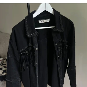 Svart jacka med fransar från Zara - Säljer en svart jacka från Zara med coola fransdetaljer både fram och bak. Jackan har en avslappnad stil med knappar framtill och är perfekt för en edgy look. Bilderna är lånade och tror storleken är runt 152-160?? Passar större!! Kan ge egna bilder!