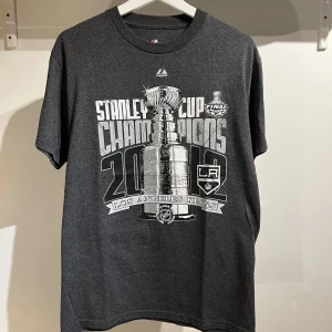 Los angels kings Champions 2012 M - La kings Champions t-shirt 2012 grå. Mycket bra skick inga defekter. Storlek Medium se mått: bräd 48cm längd 71cm. Märke majestic. Priset kan diskuteras!